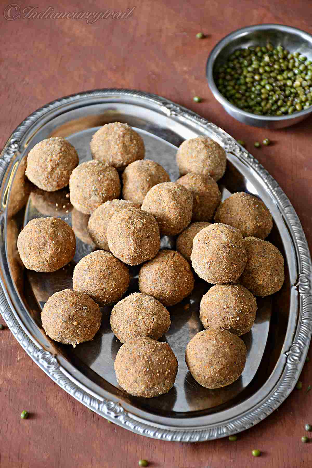 side view of green moong dal laddus kept on a plate with a bowl green moong dal behind.