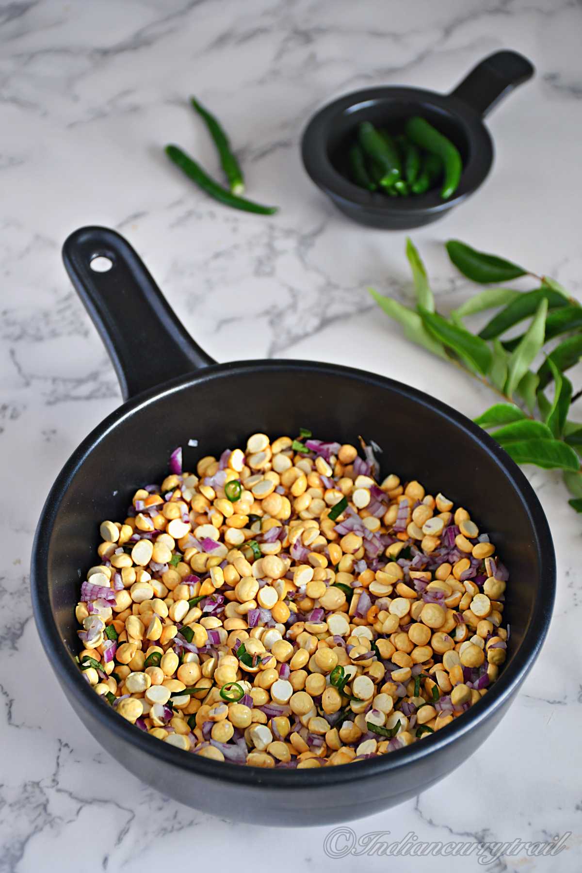 a bowl full of roasted chana dal with chopped onion and green chilli and curry leaves in the back