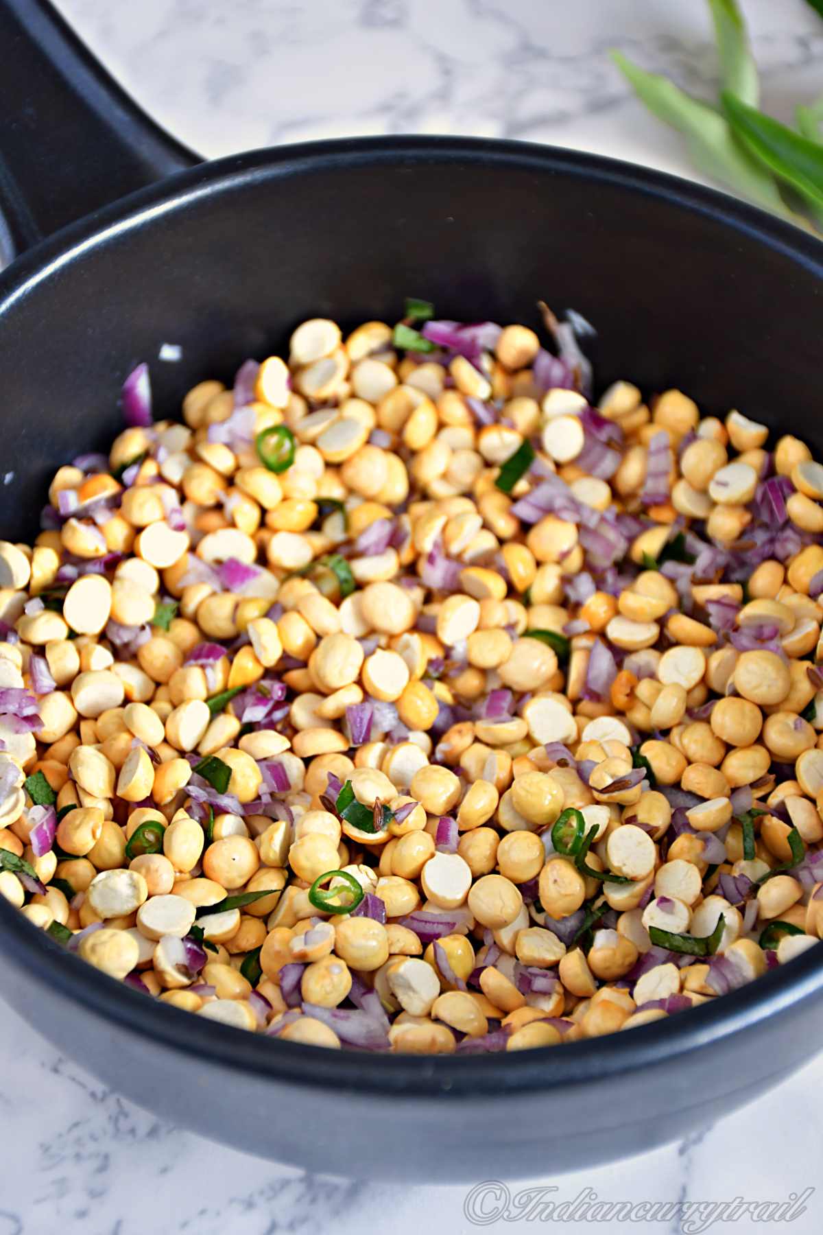 closeup picture of roasted chana dal with chopped shallots, green chilli and curry leaves and couple of curry leaves kept in the back