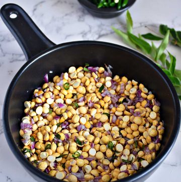 a black bowl of roasted gram dal salad mixed with finely chopped shallots and garnished with green chilli and fresh curry leaves