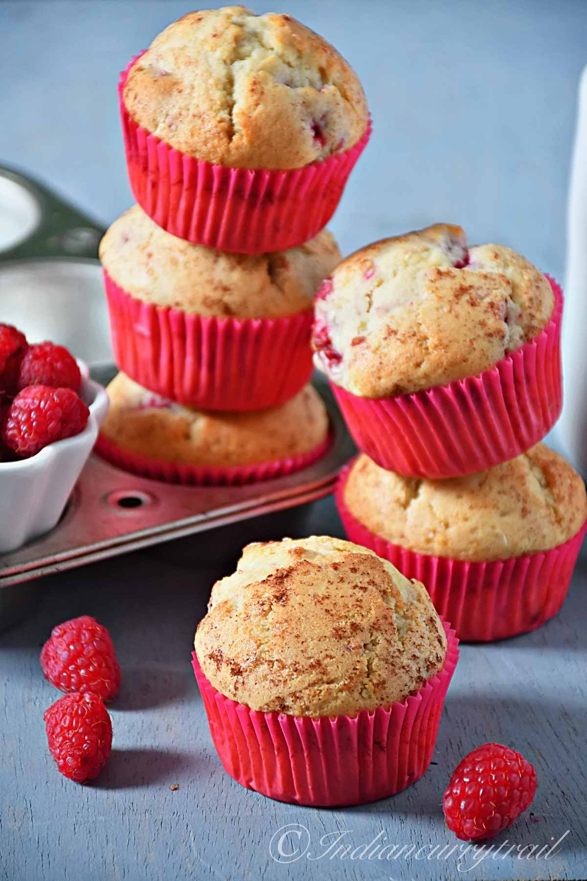raspberry muffins stacked on top of each other with some fresh raspberries scattered around
